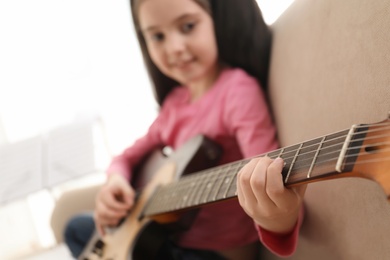 Little girl playing guitar at home, closeup. Learning music notes