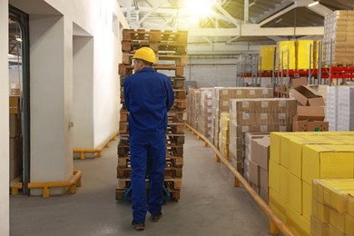 Worker moving wooden pallets with manual forklift in warehouse, back view