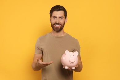 Happy man with ceramic piggy bank on orange background