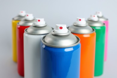Colorful cans of spray paints on light grey background, closeup