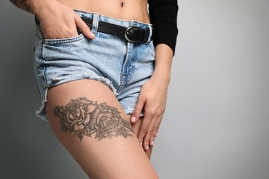 Beautiful woman with tattoos on leg against grey background, closeup. Space for text