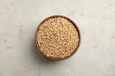 Uncooked green buckwheat grains in bowl on table, top view