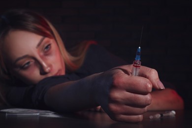 Drug addicted woman with syringe at table, focus on hand