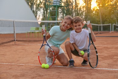 Cute children with tennis rackets and balls on court outdoors
