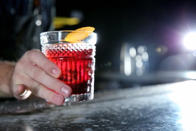 Barman holding fresh alcoholic Red Russian cocktail on bar counter, closeup. Space for text