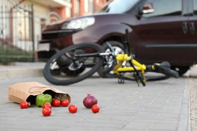 Fallen bicycle after car accident outdoors, focus on scattered vegetables