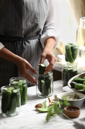 Woman putting cucumbers into jar in kitchen, closeup. Canning vegetables