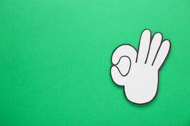 Photo of Paper cutout of okay hand gesture on green background, top view. Space for text
