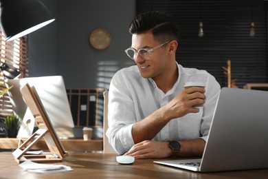 Freelancer with cup of coffee working at table indoors