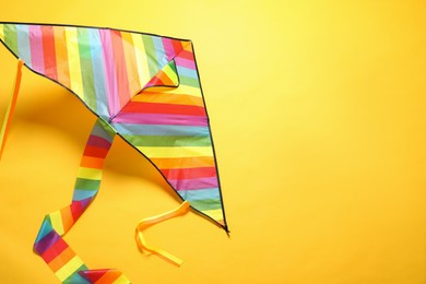Bright rainbow kite on yellow background, above view. Space for text