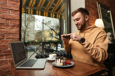 Photo of Male blogger taking photo of dessert and coffee at table in cafe