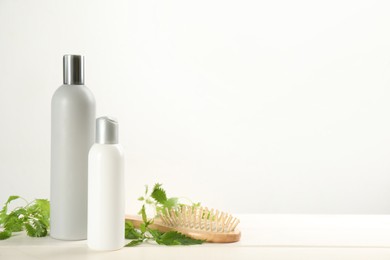 Stinging nettle, cosmetic products and brush on white wooden background, space for text. Natural hair care