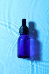 Bottle of face serum in water on light blue background, top view
