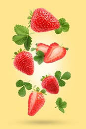 Image of Delicious sweet strawberries and green leaves falling on pale yellow background