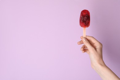 Woman holding delicious ice pop on light purple background, closeup view with space for text. Fruit popsicle