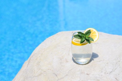 Refreshing water with lemon and mint on rock near swimming pool outdoors, space for text