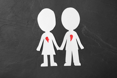 Human paper figures with parted heart on black stone background, flat lay. Composition symbolizing problems in relationship