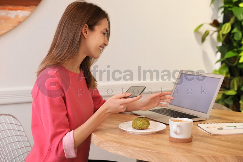 Young blogger taking photo of dessert at table in cafe
