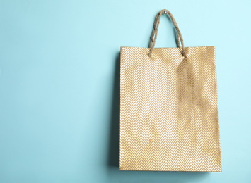 Gold shopping paper bag on light blue background, space for text