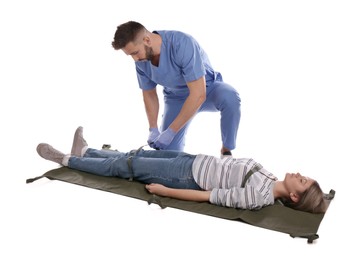 Doctor in uniform fixing woman on stretcher 
against white background. First aid