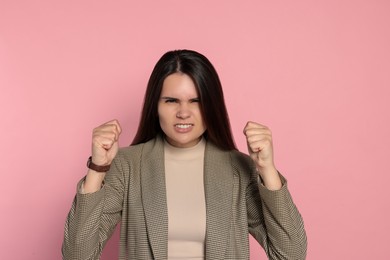 Aggressive young woman showing fists on pink background