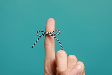 Woman showing index finger with tied bow as reminder on light blue background, closeup