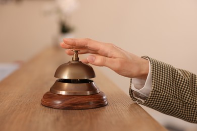 Photo of Woman ringing hotel service bell at wooden reception desk, closeup