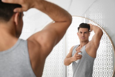 Handsome man applying deodorant to armpit near mirror in bathroom