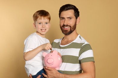 Father and his son with ceramic piggy bank on beige background