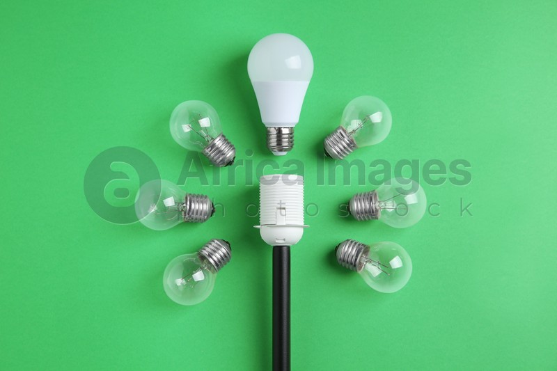 LED light bulb and simple ones near socket on green background, flat lay. Energy saving concept