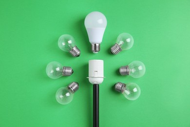 Photo of LED light bulb and simple ones near socket on green background, flat lay. Energy saving concept