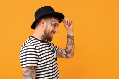 Photo of Smiling hipster man wearing stylish hat on orange background. Space for text