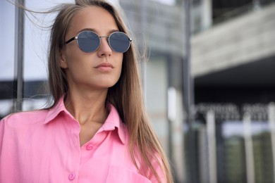 Photo of Beautiful young woman in stylish sunglasses on city street, space for text