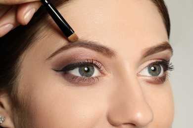 Artist correcting woman's eyebrow shape with powder on grey background, closeup