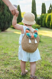 Cute little girl in stylish clothes holding mother's hand outdoors on sunny day, back view