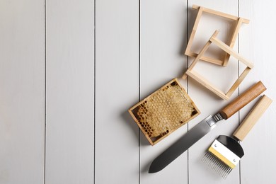 Photo of Honeycomb frame and beekeeping tools on white wooden table, flat lay. Space for text