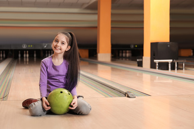 Little girl with ball in bowling club. Space for text