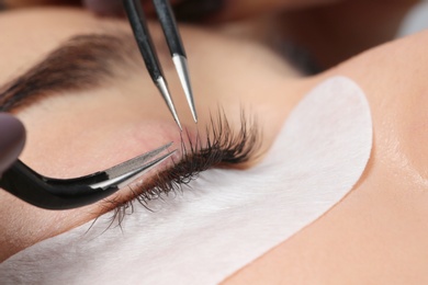 Young woman undergoing eyelashes extensions procedure, closeup