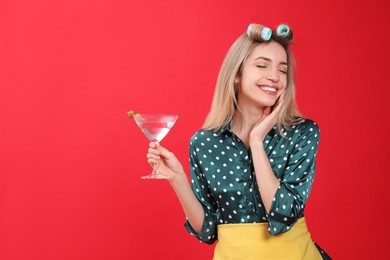 Young housewife with glass of martini on red background. Space for text
