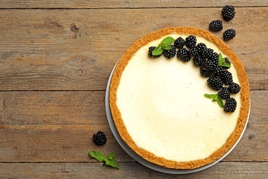 Delicious cheesecake decorated with blackberries on wooden table, flat lay. Space for text