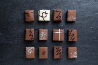 Different delicious chocolate candies on black table, flat lay
