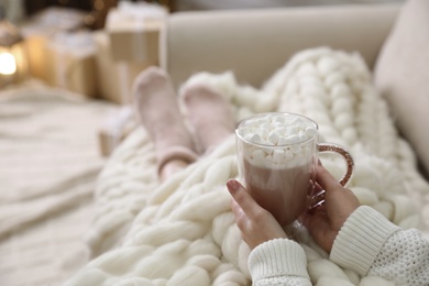 Photo of Woman with delicious hot drink wrapped in plaid on sofa at home, closeup. Space for text