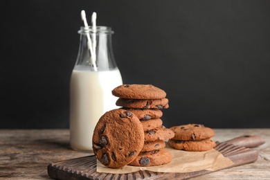 Stack of tasty chocolate chip cookies and bottle of milk on wooden table