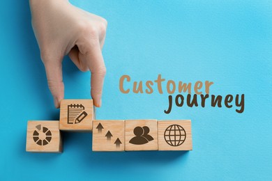 Image of Woman arranging wooden cubes with different images on light blue background, top view. Customer journey concept