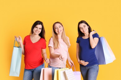 Happy pregnant women with shopping bags on orange background