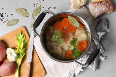 Pot of delicious vegetable bouillon and ingredients on light grey table, flat lay