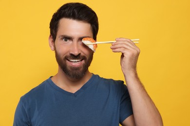 Photo of Funny man holding sushi with chopsticks on orange background