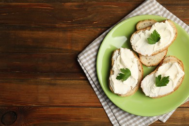 Bread with cream cheese and parsley on wooden table, top view. Space for text