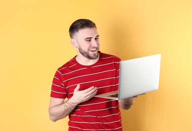 Young man using video chat on laptop against color background