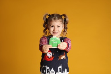 Cute little girl with Christmas gingerbread cookie on yellow background